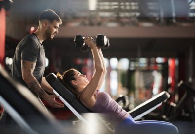 Fitness instructor assisting athletic woman in exercising with dumbbells at gym.